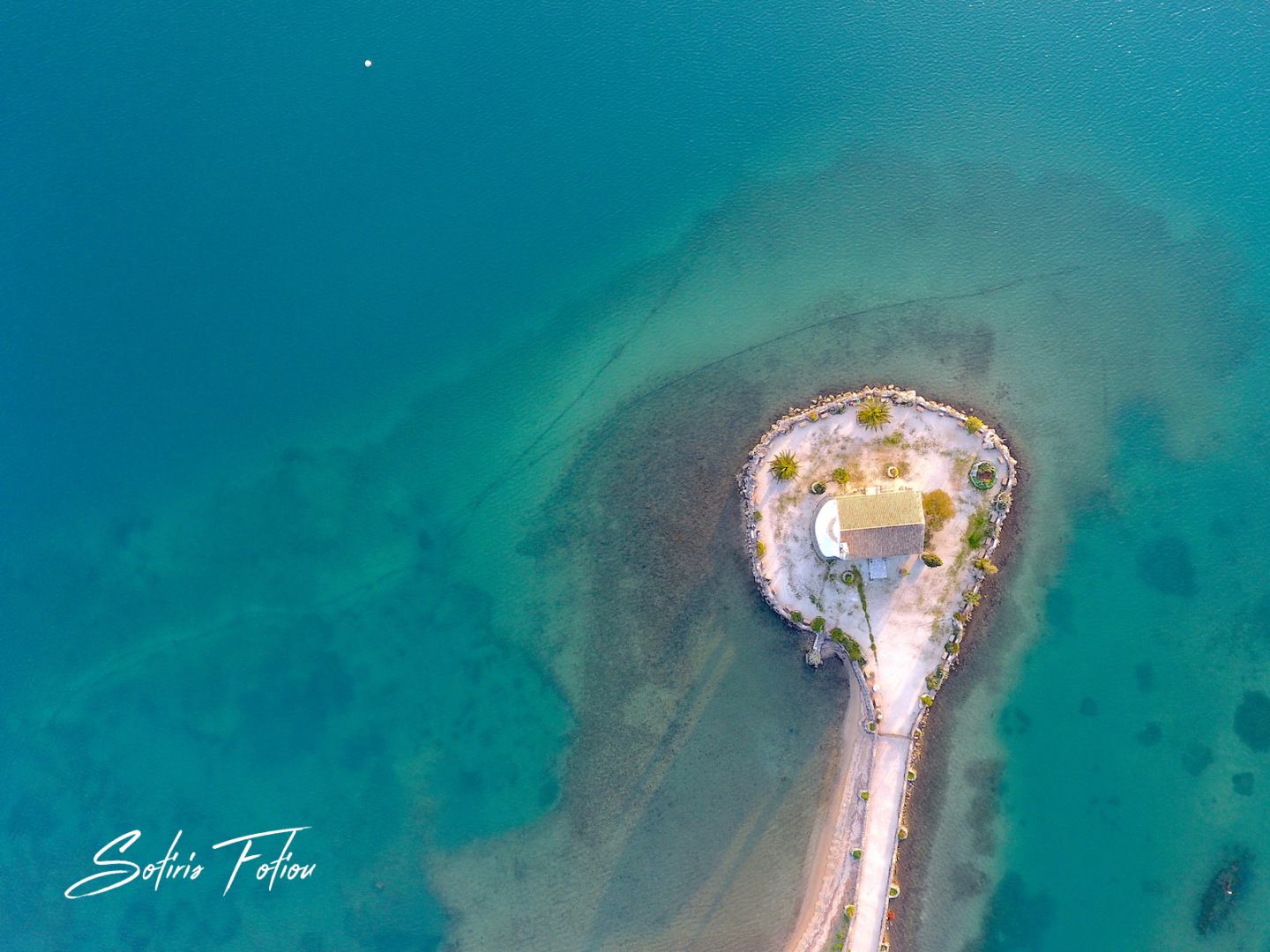 Aerial view of a small chapel on an island in Corfu's turquoise waters